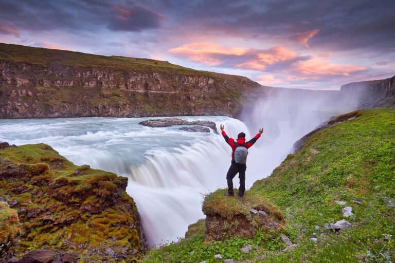 Gullfoss waterfall on the Hvíta river, a popular tourist attraction and part of the Golden Circle Tourist Route in Southwest Iceland. Man tourist in red jacket looks at the flow of falling water.