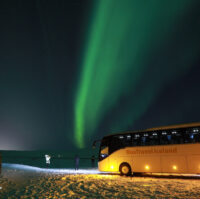 People watching the Northern Lights standing near the bus