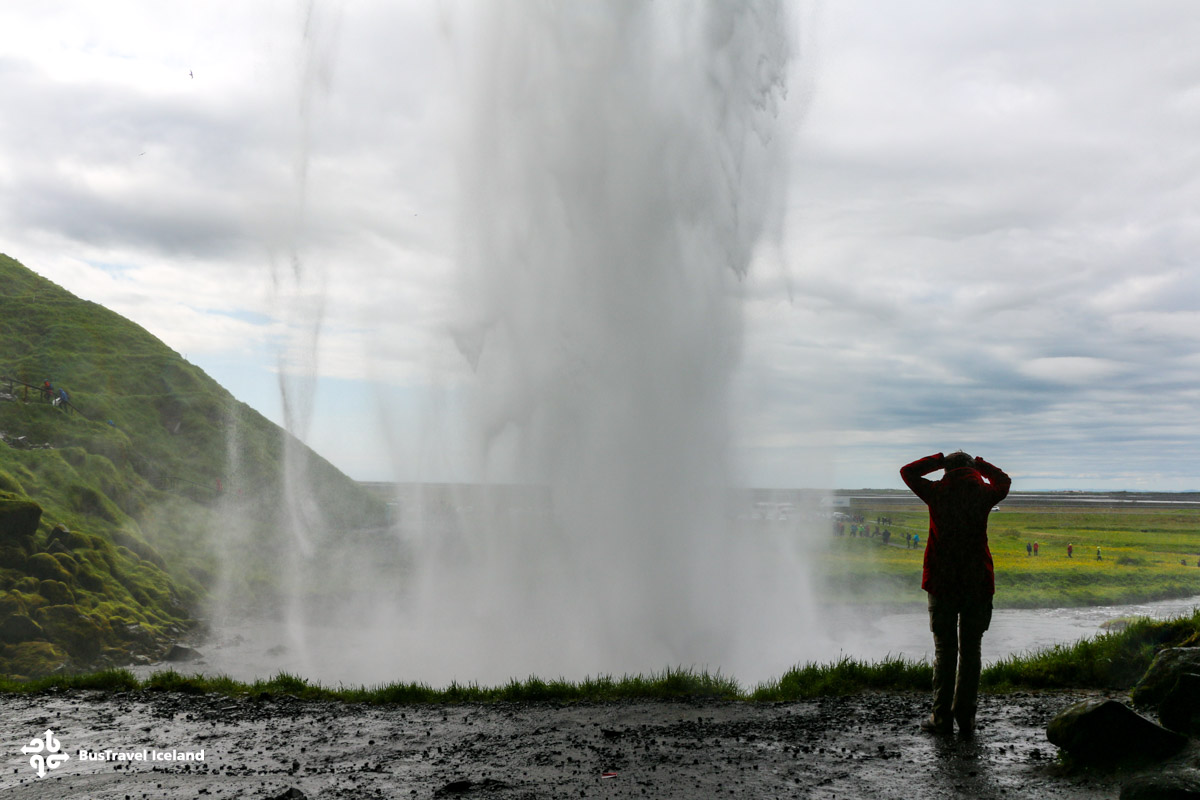 A woman standing bihind Seljalandsfoss waterfall