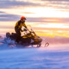 A man is riding snowmobile in mountains. Beautiful morning light. Blue shadows.