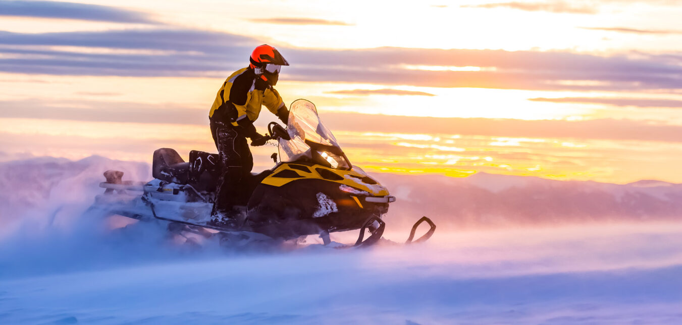 A man is riding snowmobile in mountains. Beautiful morning light. Blue shadows.
