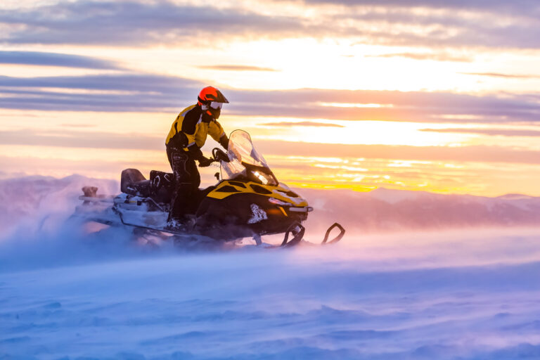 A man is riding snowmobile in mountains. Beautiful morning light. Blue shadows.