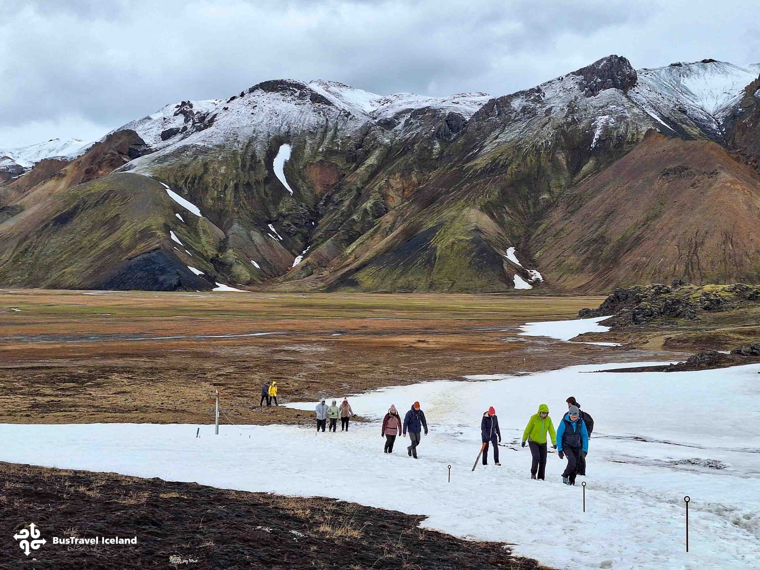 Hikers walking across a snow-covered patch in the Landmannalaugar highlands of Iceland